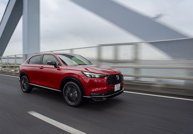 ホンダ・ヴェゼル e:HEV RS(FF)/価格:374万8800円。RSは専用セッティングのパワーステアリングとスポーツサスペンションで気持ちのいい走りを追求。車高は標準車比−45㎜の1545㎜。車高ダウンの内訳はサスペンション分が15㎜、アンテナ分が30㎜。RSは一般的な立体駐車場に対応する